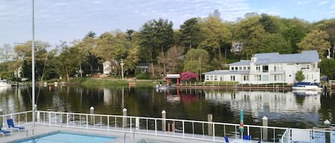 A swimming pool with lounge chairs, a dock with boats, and a large house with a view of the water.
