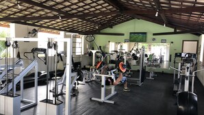 A gym with various exercise equipment, a mirrored wall, and a green wall with a clock. - 5-bedroom house in condominium, comfort, air conditioning, 55" SmartTV, Wi-Fi, pool, lagoon, beach. (Vilas do Atlântico)