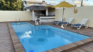 A rectangular swimming pool with a wooden deck surrounding it. There are lounge chairs and a yellow umbrella. - 5-bedroom house in condominium, comfort, air conditioning, 55" SmartTV, Wi-Fi, pool, lagoon, beach. (Vilas do Atlântico)