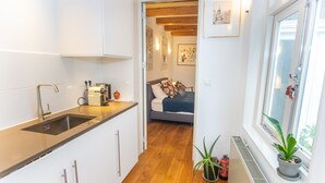 A compact kitchen with a modern sink and cabinets, a small dining area, and a bedroom with a bed and pillows.