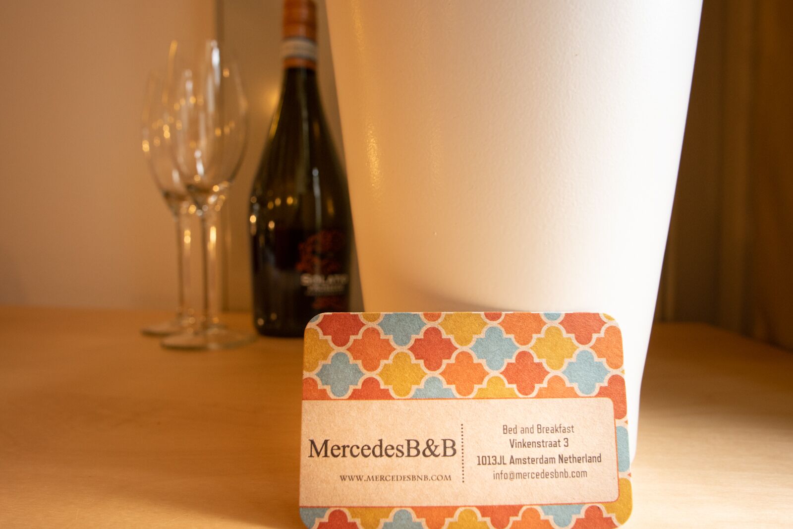 Een hotelkamer met een tafel waarop een wijnfles en glazen staan, en een kleurrijk kaartje met hotelinformatie.