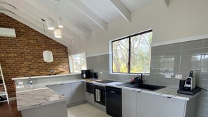 Une cuisine moderne dotée d’un grand îlot central, de meubles blancs et d’un mur d’accent en briques.