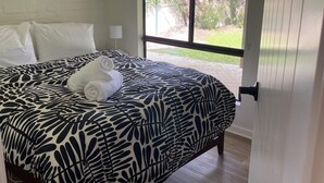 Une chambre à coucher avec un grand lit, des oreillers blancs, une couvre-lit à motifs, une lampe de chevet et une vue sur un jardin par la fenêtre.
