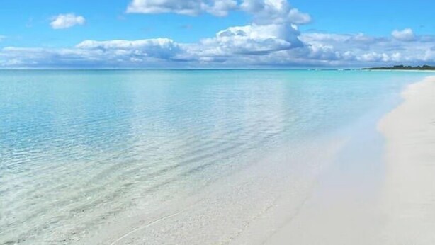 Une plage à l’eau turquoise et limpide, bordée d’un rivage sablonneux.