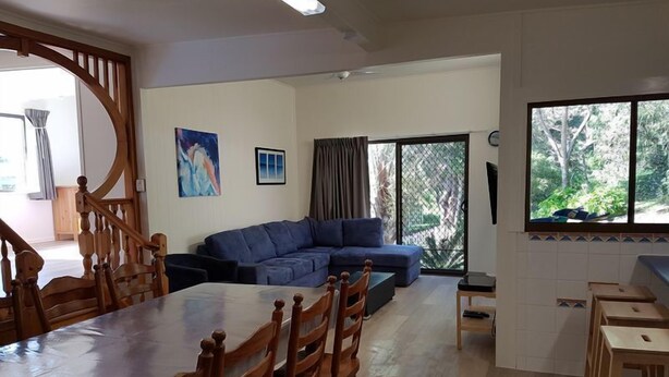 A spacious living area with a large wooden dining table, blue sofa, and a view of greenery through a window. - Lil's Place - Happy Valley - K'gari (Fraser Island) (Fraser Island)
