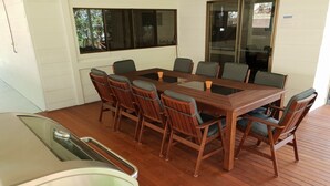 A wooden deck with a dining table and chairs, a grill, and a window with a view of trees. - Lil's Place - Happy Valley - K'gari (Fraser Island) (Fraser Island)