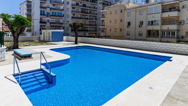 Una piscina rectangular con superficie de agua cristalina y azul, rodeada por una terraza empavedada.