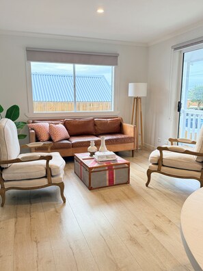 Un salon comprenant un canapé, deux fauteuils, une table basse et une fenêtre avec des stores.