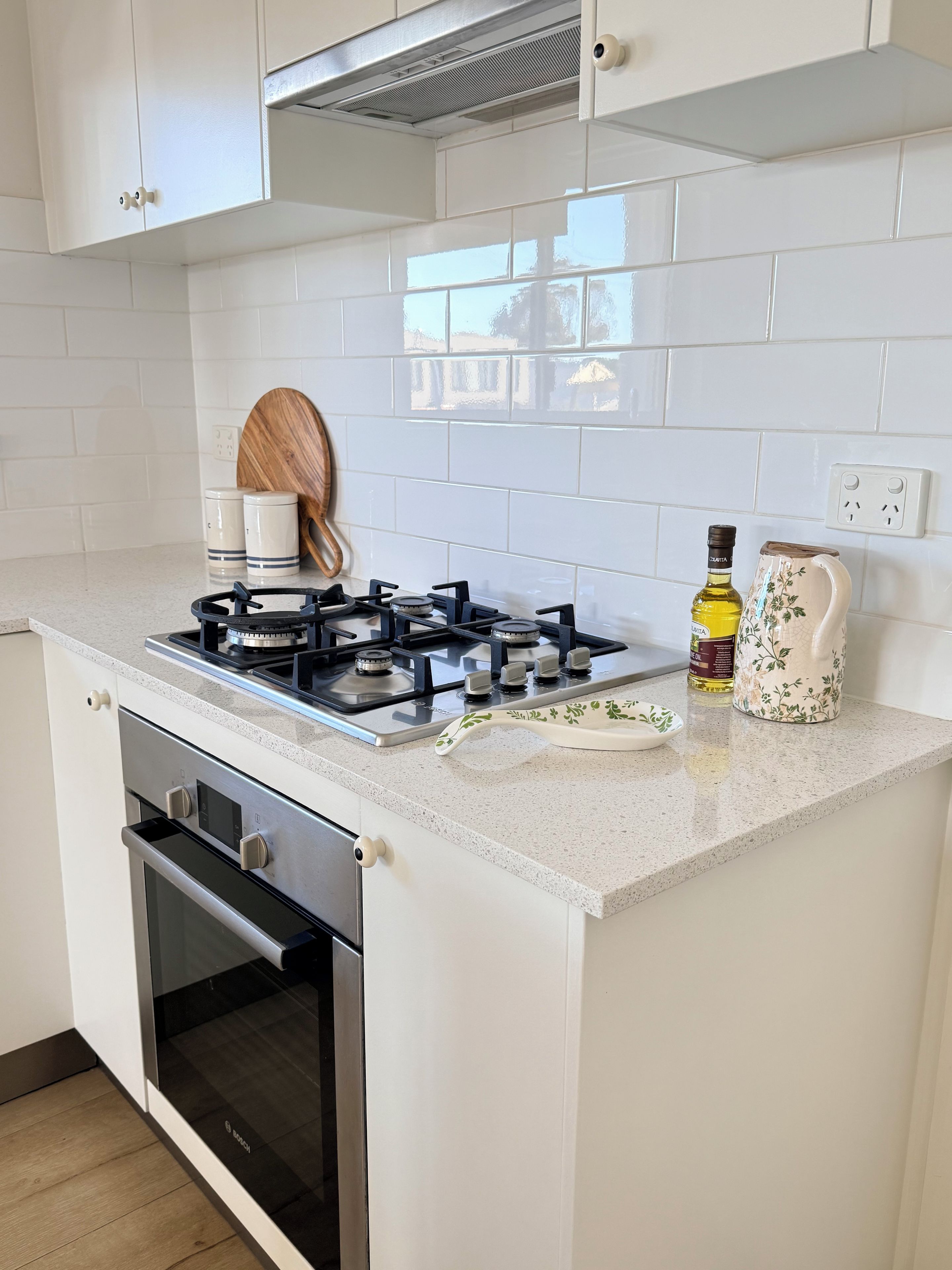 A kitchen with white cabinets, a stove, an oven, and a countertop with a bottle and a decorative plate.