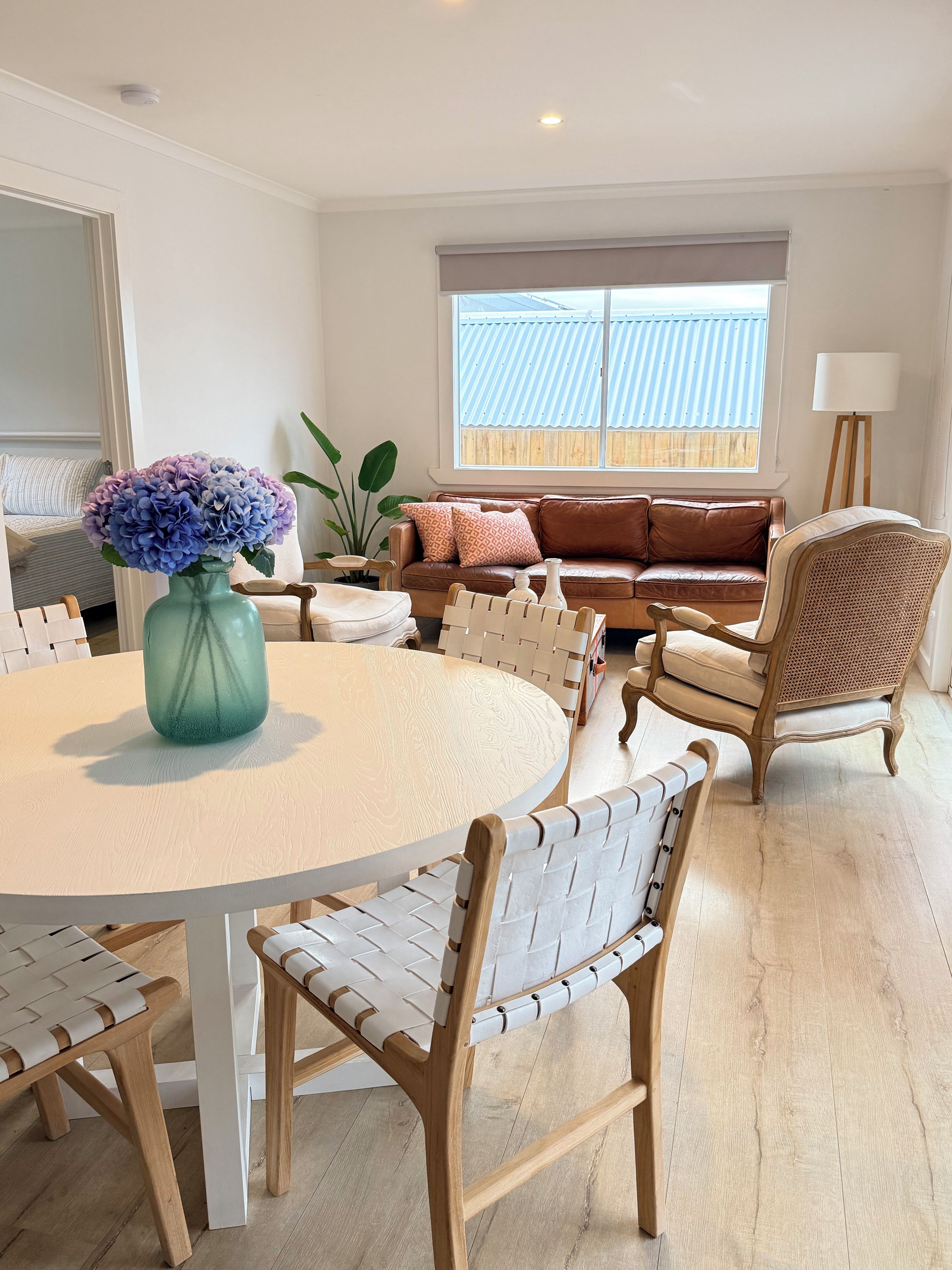 A modern living room with a round table, leather sofa, and wicker chairs.