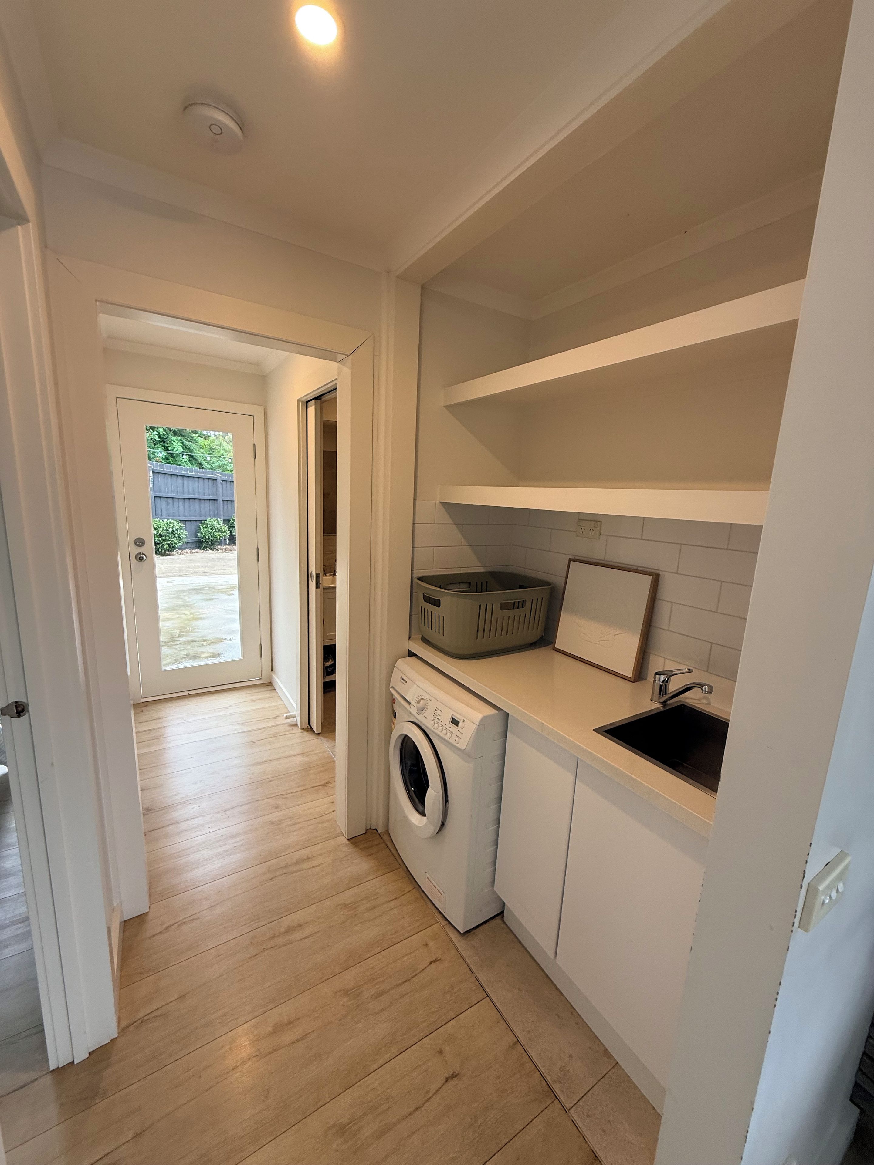 Une buanderie équipée d’un lave-linge, d’un évier et d’un panier posé sur un plan de travail.