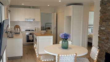 A modern kitchen with white cabinets, a dining area with a round table and wicker chairs, and a stone accent wall.