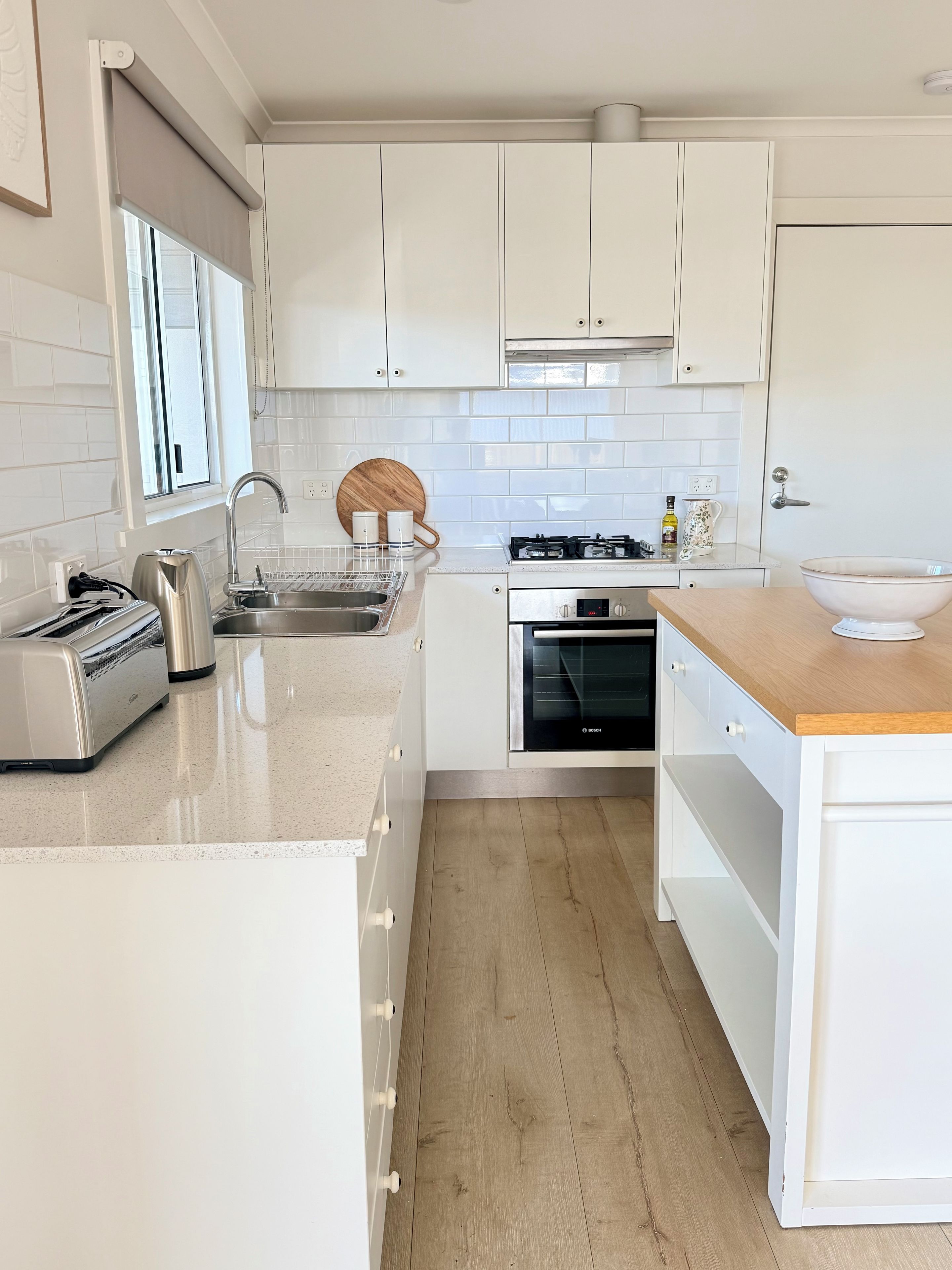 A modern kitchen with white cabinetry, a Bosch oven, a stainless steel sink, and a wooden countertop.