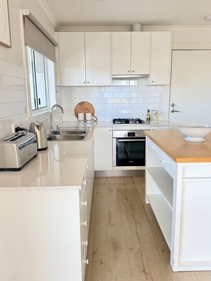 A modern kitchen with white cabinetry, a Bosch oven, a stainless steel sink, and a wooden countertop.