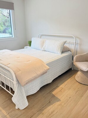 A bed with a white metal frame, a beige blanket, and striped bedding.