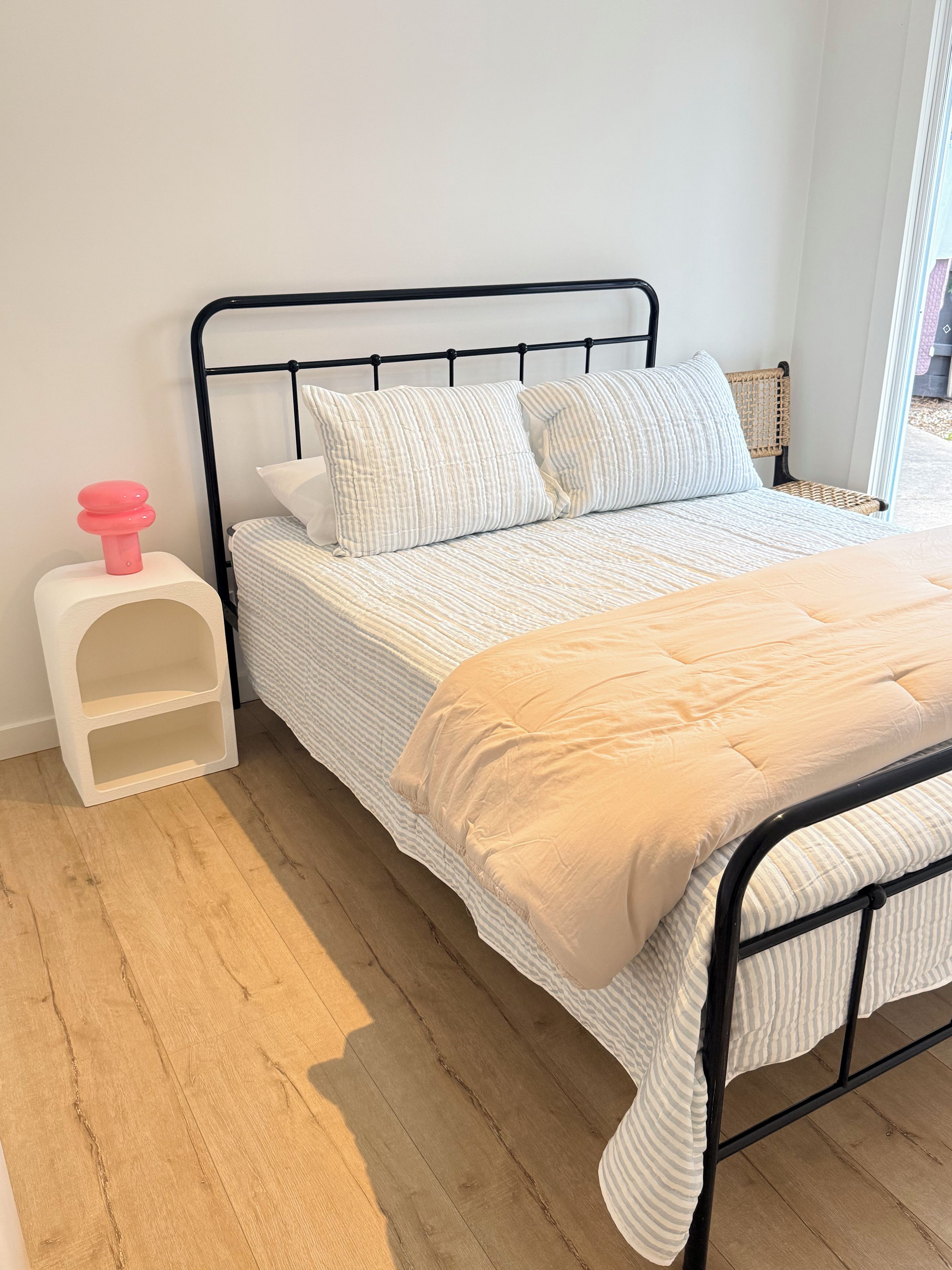 A bed with a striped bedding, a white pillow, and a beige throw.