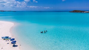Une plage avec une eau turquoise et limpide, un rivage sablonneux et quelques personnes qui se baignent.
