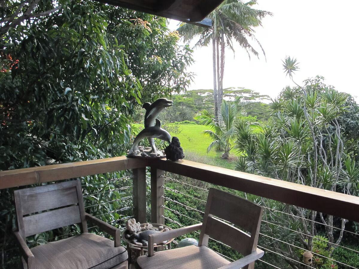 A balcony with a view of a lush garden, a wooden chair, and a decorative bird sculpture.