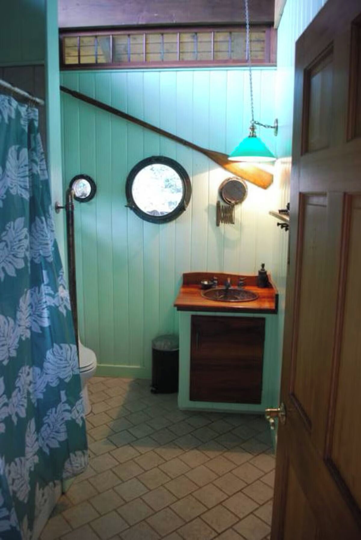 Un baño con lavamanos de madera, inodoro, cortina de ducha y lámpara colgante.
