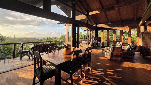 Une vaste terrasse en bois, dotée d’une table et de chaises, de grandes fenêtres et offrant une vue sur le paysage.