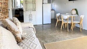 Een moderne woonkamer met een bank, een eettafel met stoelen, een keuken met een koelkast, en een televisie aan de muur.