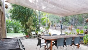 An outdoor patio with a wooden table and chairs, surrounded by greenery and a covered area. - K'GARI (FRASER ISLAND) My Island Home. Sleeps 14. Situated in Eurong  (Eurong)