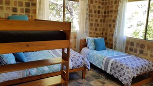 A room with two wooden beds, a window with curtains, and a brick-patterned wall. - K'GARI (FRASER ISLAND) My Island Home. Sleeps 14. Situated in Eurong  (Eurong)