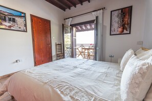 Een slaapkamer met een bed, een houten deur, een raam en een balkon met stoelen en een tafel.