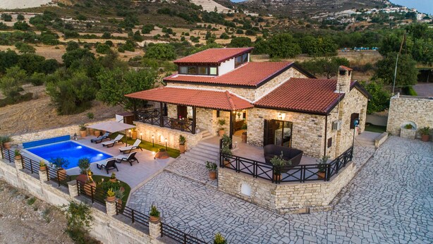 Una villa de piedra con piscina, mobiliario exterior y vistas del paisaje circundante.