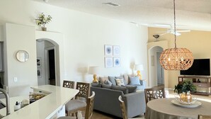 Eine moderne Küche mit einer zentralen Kochinsel, einem Essbereich mit Stühlen, einer Couch und einem Fernseher.