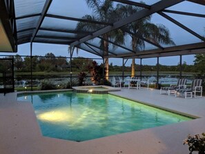 Una piscina interior con techo de cristal, rodeada de sillones de descanso y vistas a un lago y árboles.