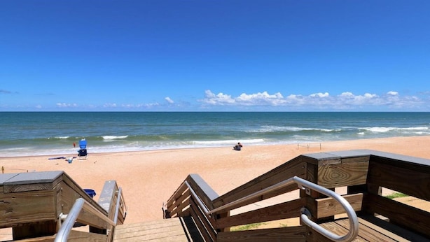A wooden deck leading to a beach with a clear view of the ocean and a person in the water.