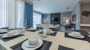 Ein moderner Essbereich mit Tisch für vier Personen, einem Fernseher im Hintergrund und einem Sofa im Wohnzimmer.