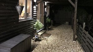 Una cabaña de madera con camino de grava, un porche cubierto y una maceta colgante cerca de la entrada.