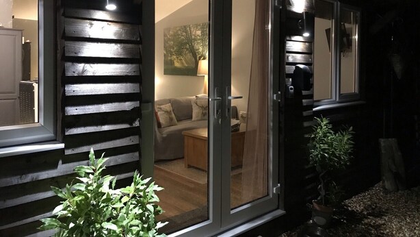 Una habitación acogedora con puerta corrediza de vidrio que da a una sala de estar, pared exterior de madera y una planta en maceta.