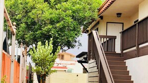 A residential area with a staircase leading to a house, surrounded by greenery and a clear sky.
