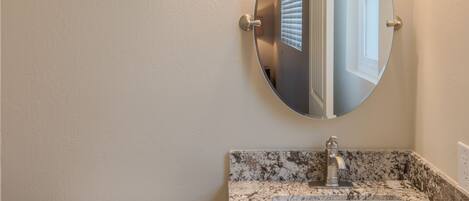 A bathroom with a white toilet, a granite countertop sink, and a round mirror.