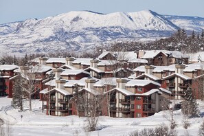 Un complejo turístico cubierto de nieve con varios edificios de dos pisos, cada uno con balcones y una pista de esquí al fondo.