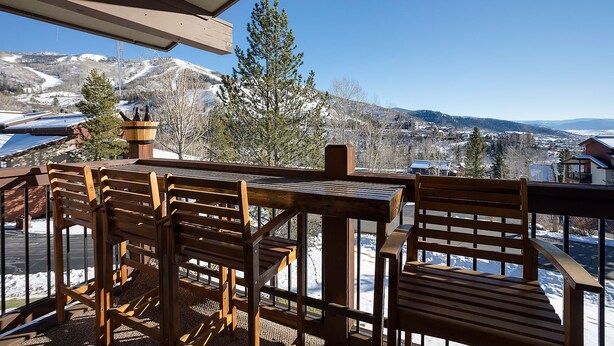 A wooden deck with a table and chairs, overlooking a snowy mountain landscape. - RA208 | Nicely Appointed Condo | Quiet setting | Winter Shuttle | Wood Fireplace (Steamboat Springs)