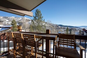 A wooden deck with a table and chairs, overlooking a snowy mountain landscape. - RA208 | Nicely Appointed Condo | Quiet setting | Winter Shuttle | Wood Fireplace (Steamboat Springs)