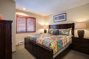 Un dormitorio con una cama de madera, dos lámparas de noche, una ventana con persianas y un cuadro en la pared.