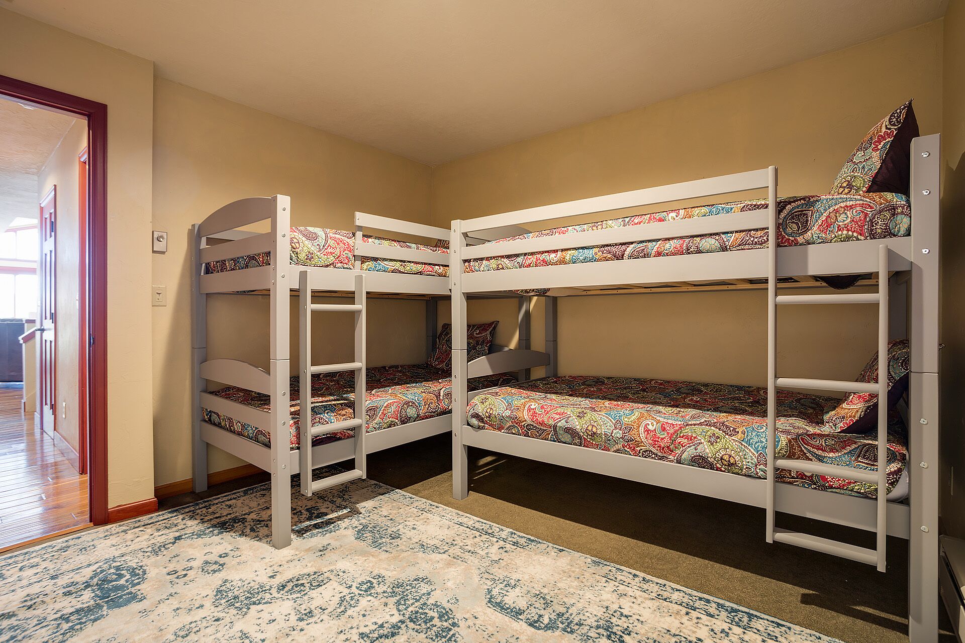 Habitación con literas, una colcha estampada, piso de madera y una puerta.