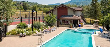 A pool area with two pools, lounge chairs, and a tennis court.