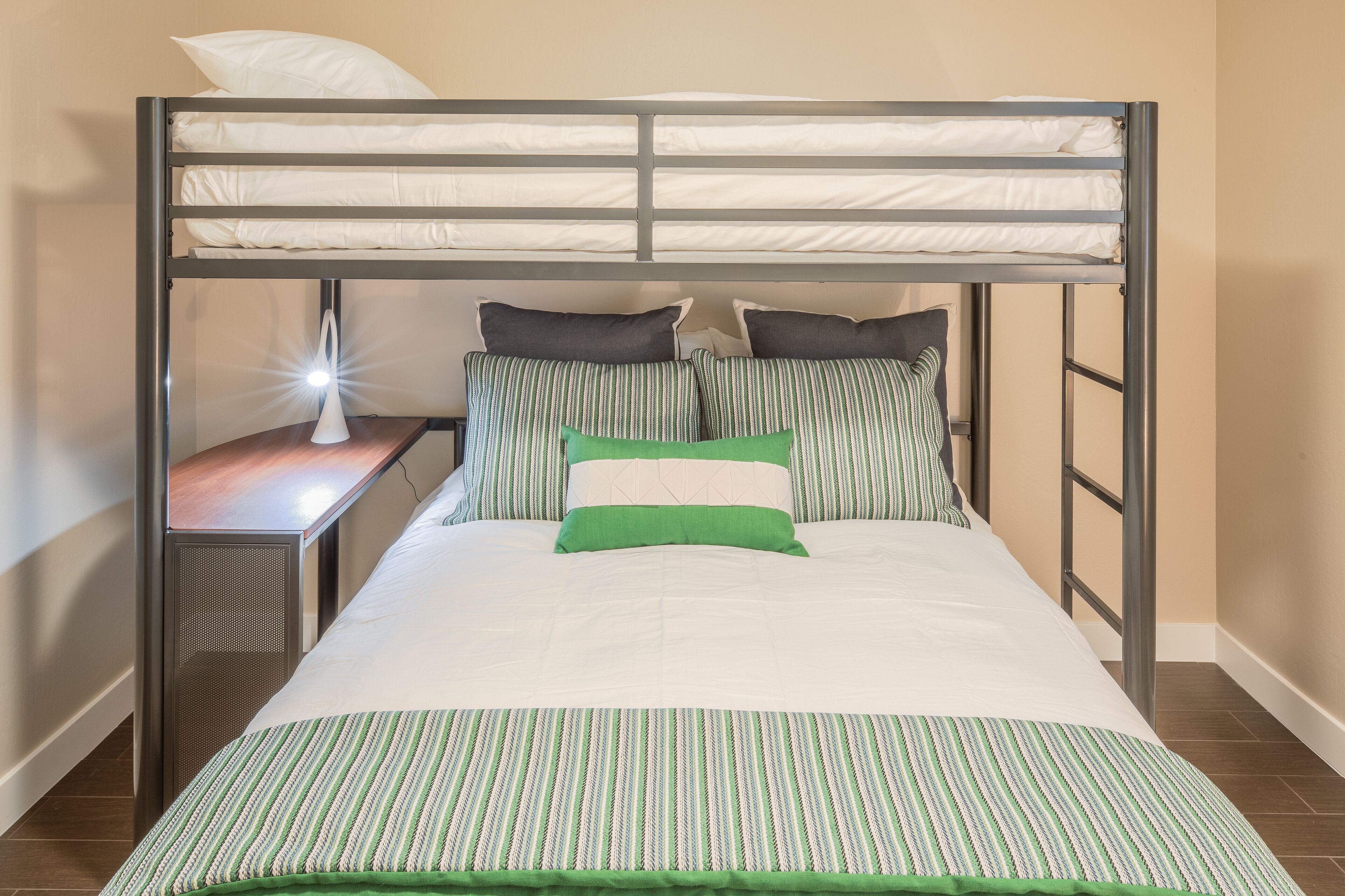A bunk bed with a desk and lamp, featuring a striped bedspread and pillows.