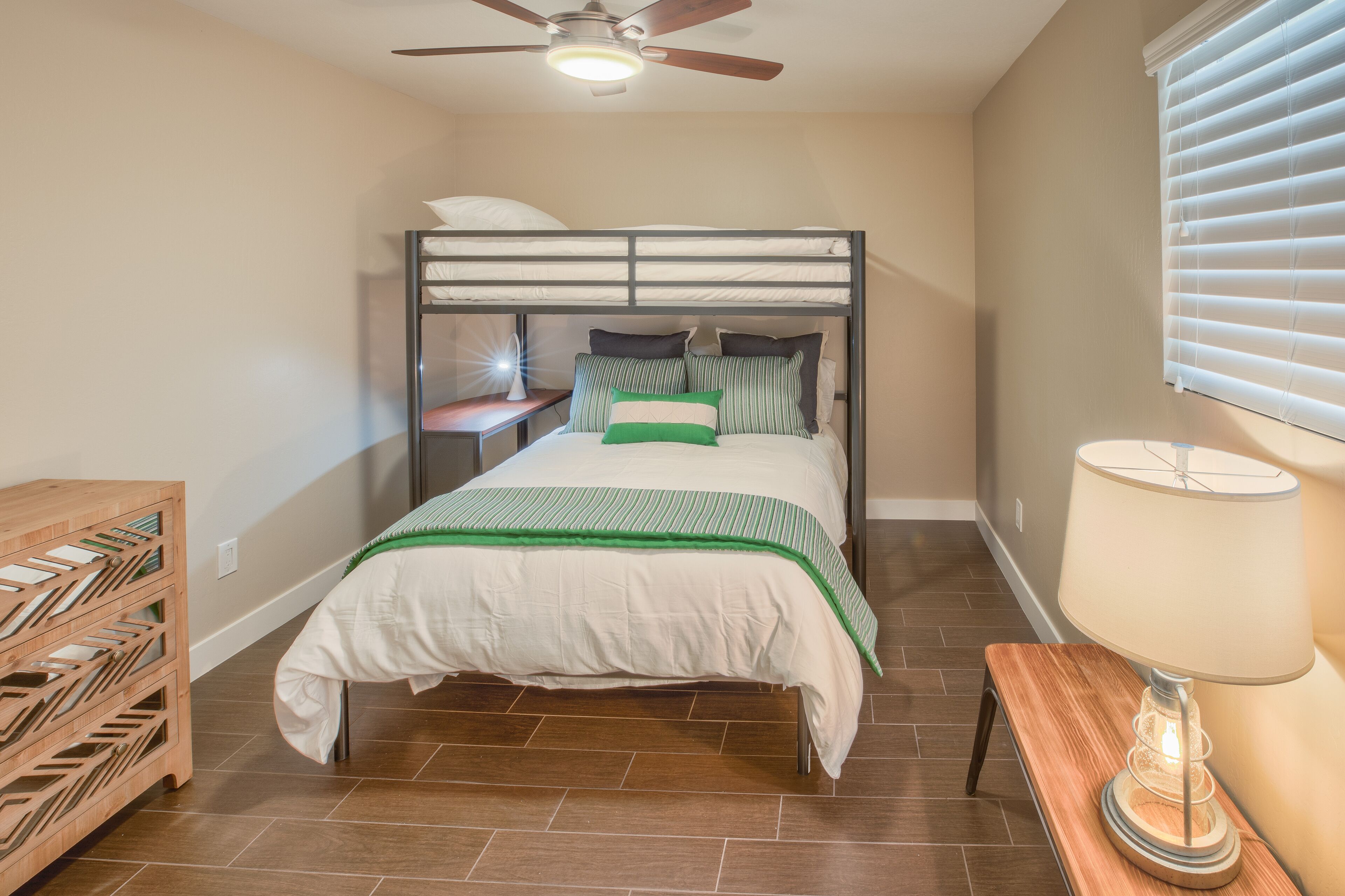 A bedroom with a bunk bed, a wooden nightstand, a lamp, and a wooden storage unit.