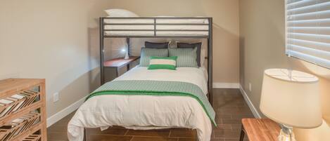 A bedroom with a bunk bed, a wooden nightstand, a lamp, and a wooden storage unit.