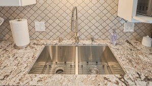 Una cocina con un lavamanos de acero inoxidable, encimera de mármol y un salpicadero con diseño.