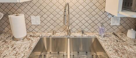A kitchen with a stainless steel sink, a marble countertop, and a patterned backsplash.