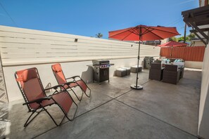 Une terrasse extérieure avec deux chaises pliantes, un barbecue et une table avec un parasol.