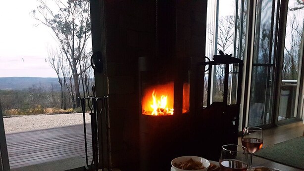A cozy room with a wood-burning stove, a dining table with a bowl of cereal and wine glasses, and a view of the outdoors.